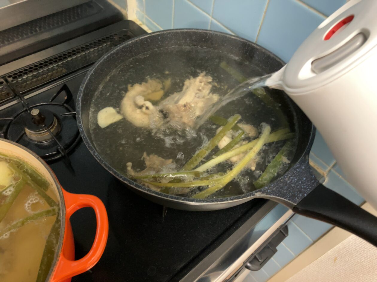 煮込んでいる鶏ガラの鍋に差し湯をしている写真