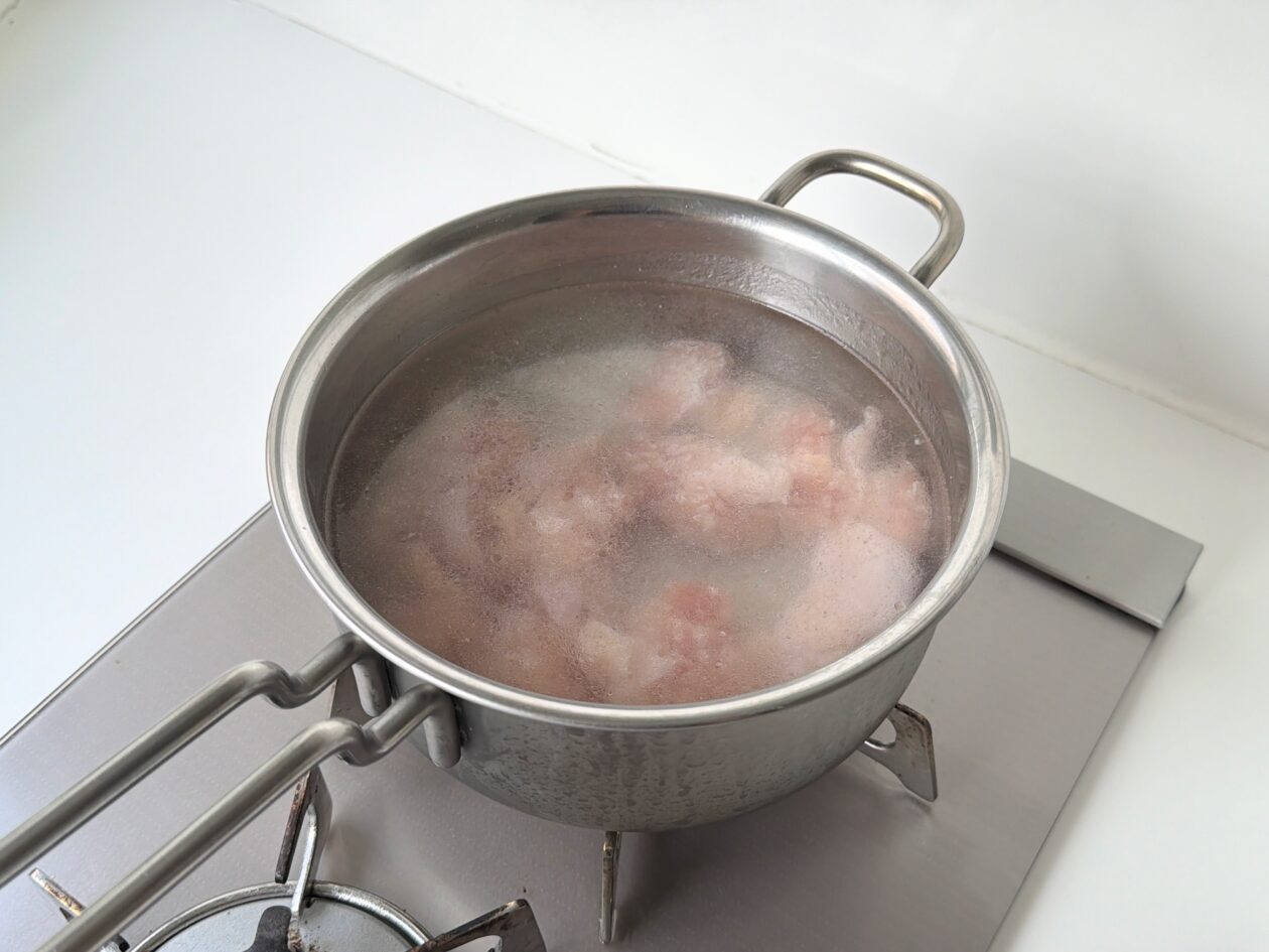 米と鶏肉を鍋底に均等にならし、中強火で鶏中華粥を加熱し始める様子